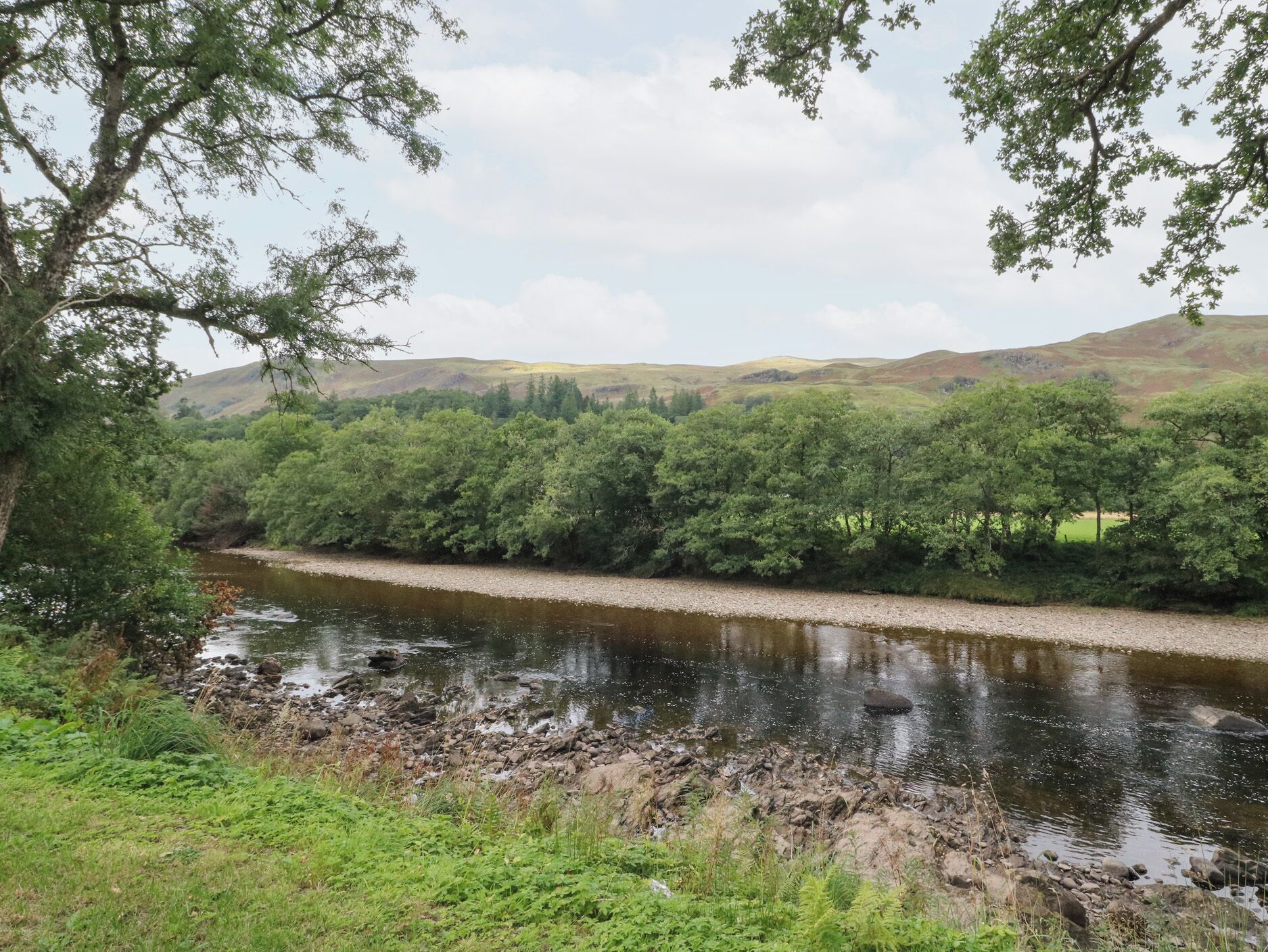 A river flowing through a valley with dense greenery and hills in the background.