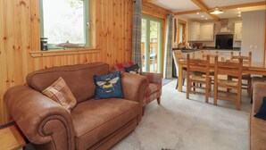 A cozy cabin interior with a brown leather sofa, plaid cushions, a dining area with wooden chairs, and a kitchen with white cabinets. - Bradan Lodge (Dalmally)