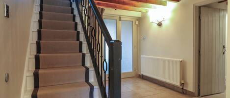 Una escalera con peldaños cubiertos de alfombra beige y barandillas negras, que conduce a una habitación con una puerta blanca y un radiador en la pared.