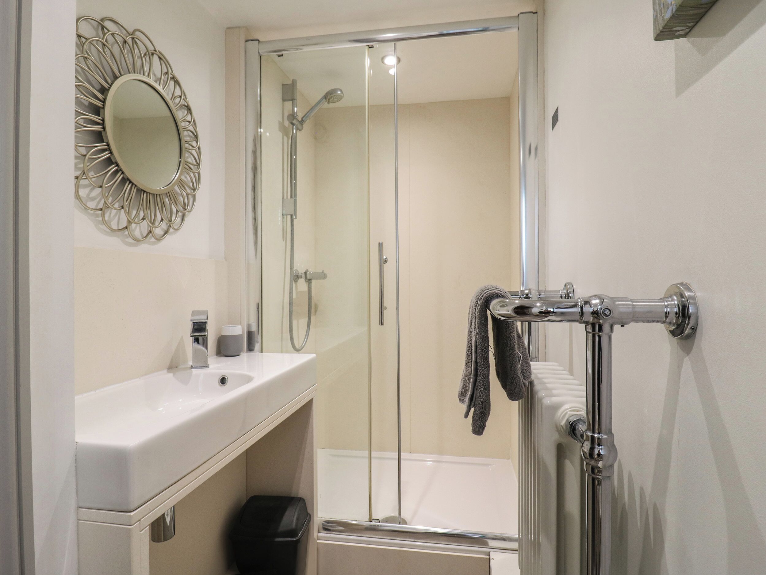 A modern bathroom with a glass shower enclosure, a white sink, and a towel rack.