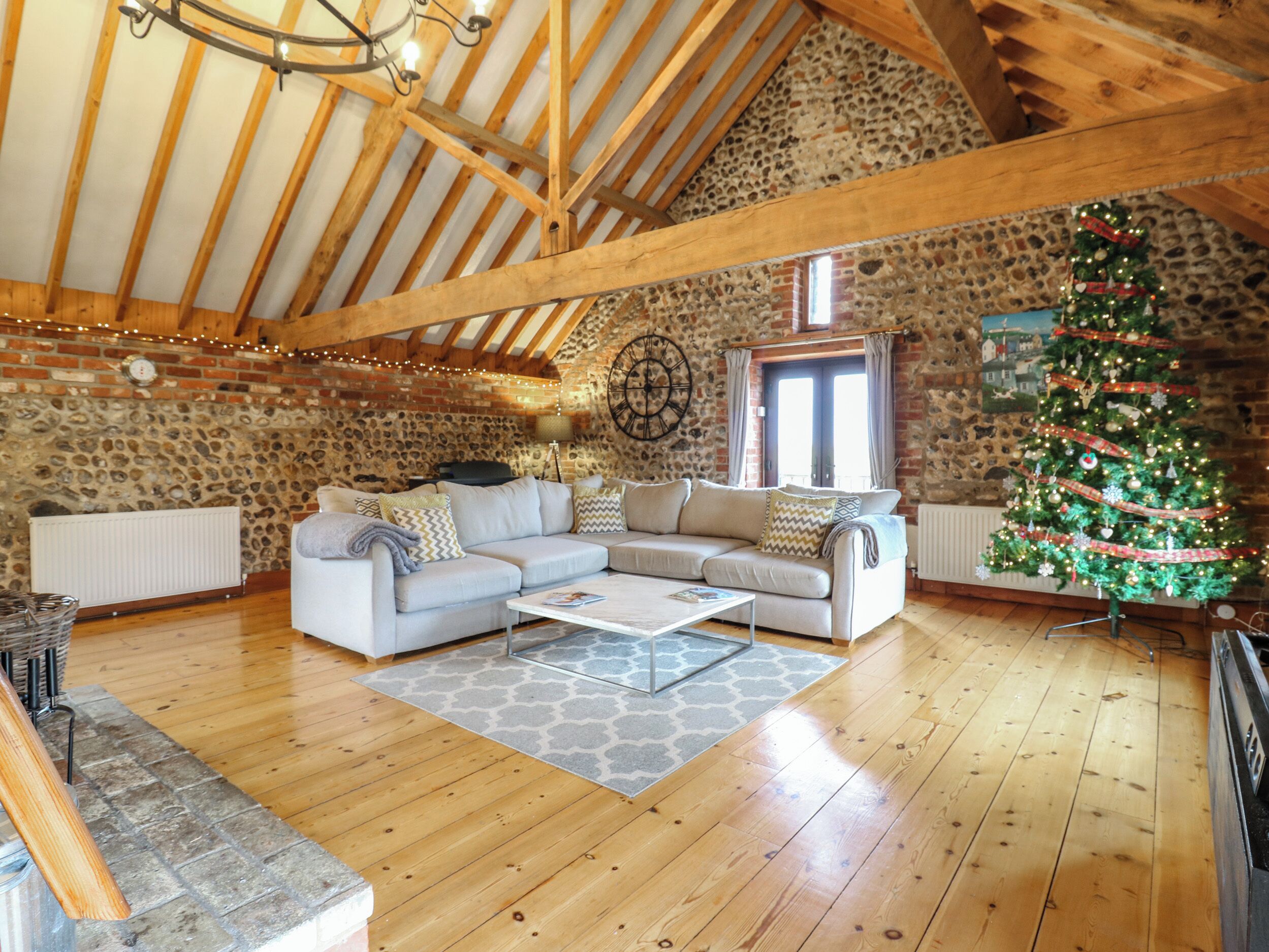 A cozy loft-style living room with a stone wall, wooden beams, a large window, and a decorated Christmas tree.