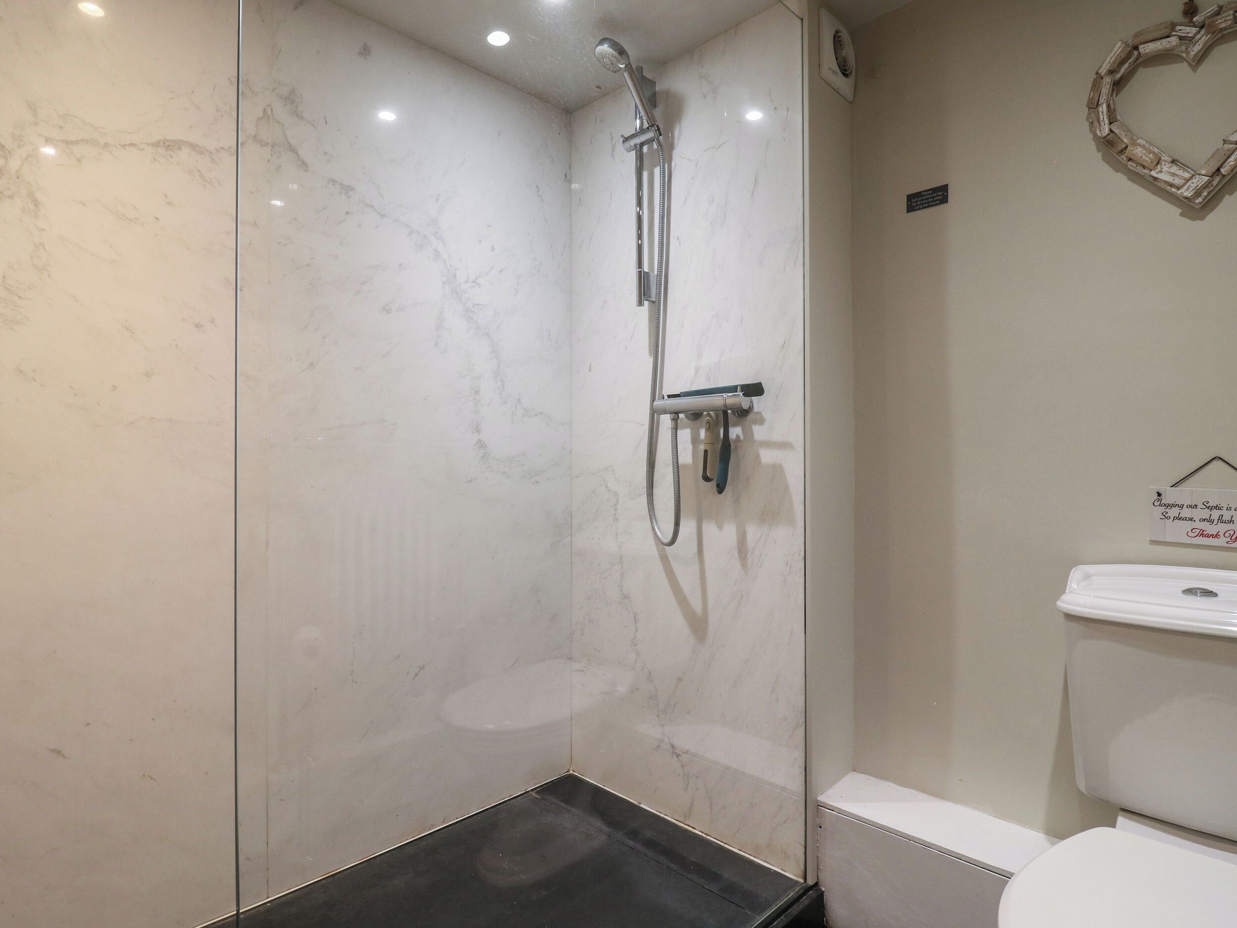 Ein modernes Badezimmer mit einer Glaskabine zur Dusche, einer weißen Toilette und einer Marmorwand.