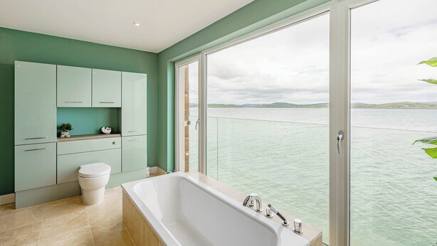 Une salle de bain avec une baignoire, des toilettes et des placards, donnant sur un plan d’eau.