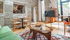 A cozy living room with a stone wall, a glass coffee table, a green sofa, and a TV stand with a flat-screen TV. - The Stables (Penzance)