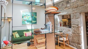 A bright living room with a green sofa, wicker furniture, and a stone wall. - The Stables (Penzance)