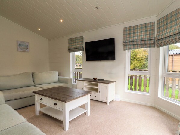 A cozy living room with a sofa, a coffee table, a TV mounted on the wall, and a window with plaid curtains.