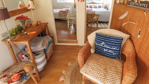 Une pièce chaleureuse avec un fauteuil en osier, une petite table avec une lampe et un lit agrémenté d’un coussin à rayures.