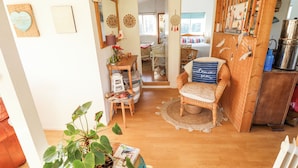 Un salon chaleureux avec un fauteuil en osier, une petite table avec des livres, une plante en pot et un meuble en bois.
