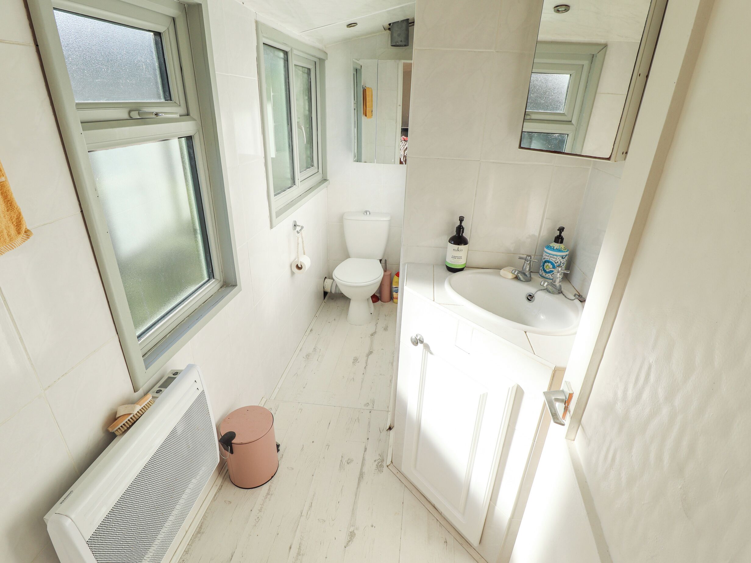 A narrow bathroom with a toilet, sink, and a window.