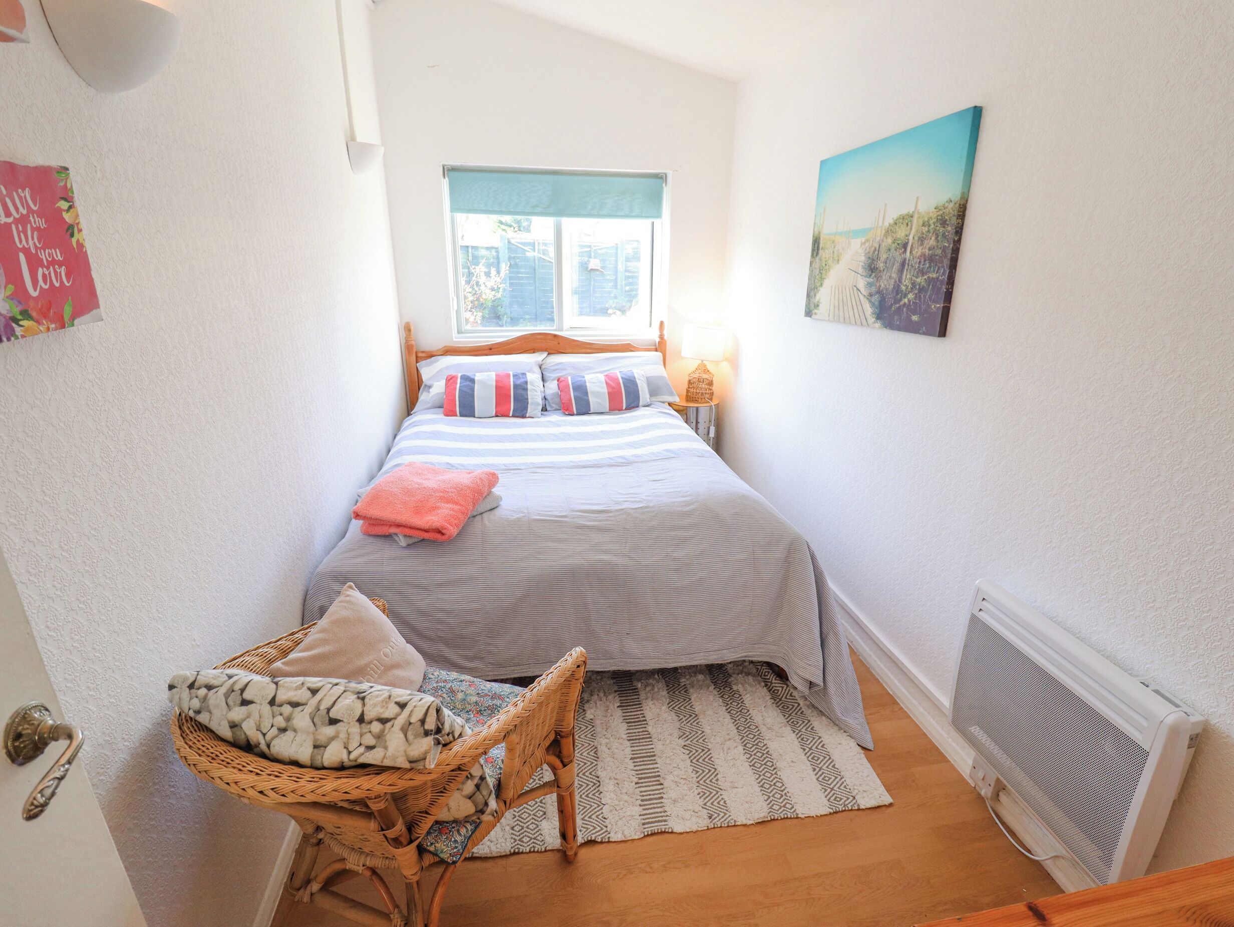 Une chambre à coucher comprenant un lit, une fenêtre, un radiateur fixé au mur, une chaise en osier et un tapis.