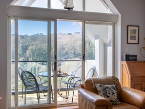 Une pièce dotée d’une porte-fenêtre coulissante donnant sur un balcon avec une table et des chaises, un canapé en cuir et un meuble en bois.