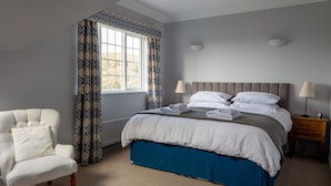A bedroom with a bed, a chair, a nightstand, and a window with curtains. - 17 St Elmo Court (Salcombe)