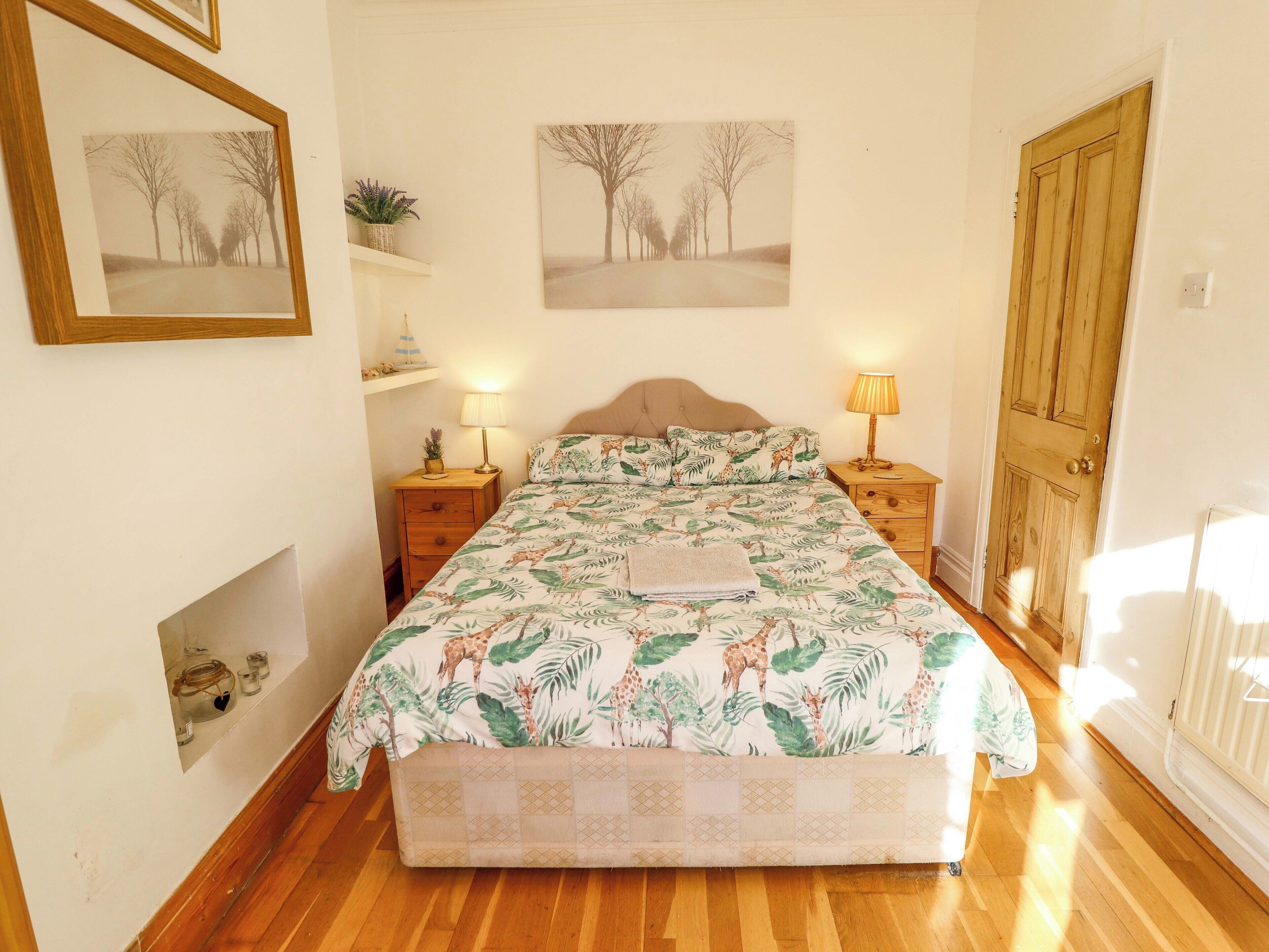 A bedroom with a bed, two bedside tables, a wooden door, and two framed pictures on the wall.