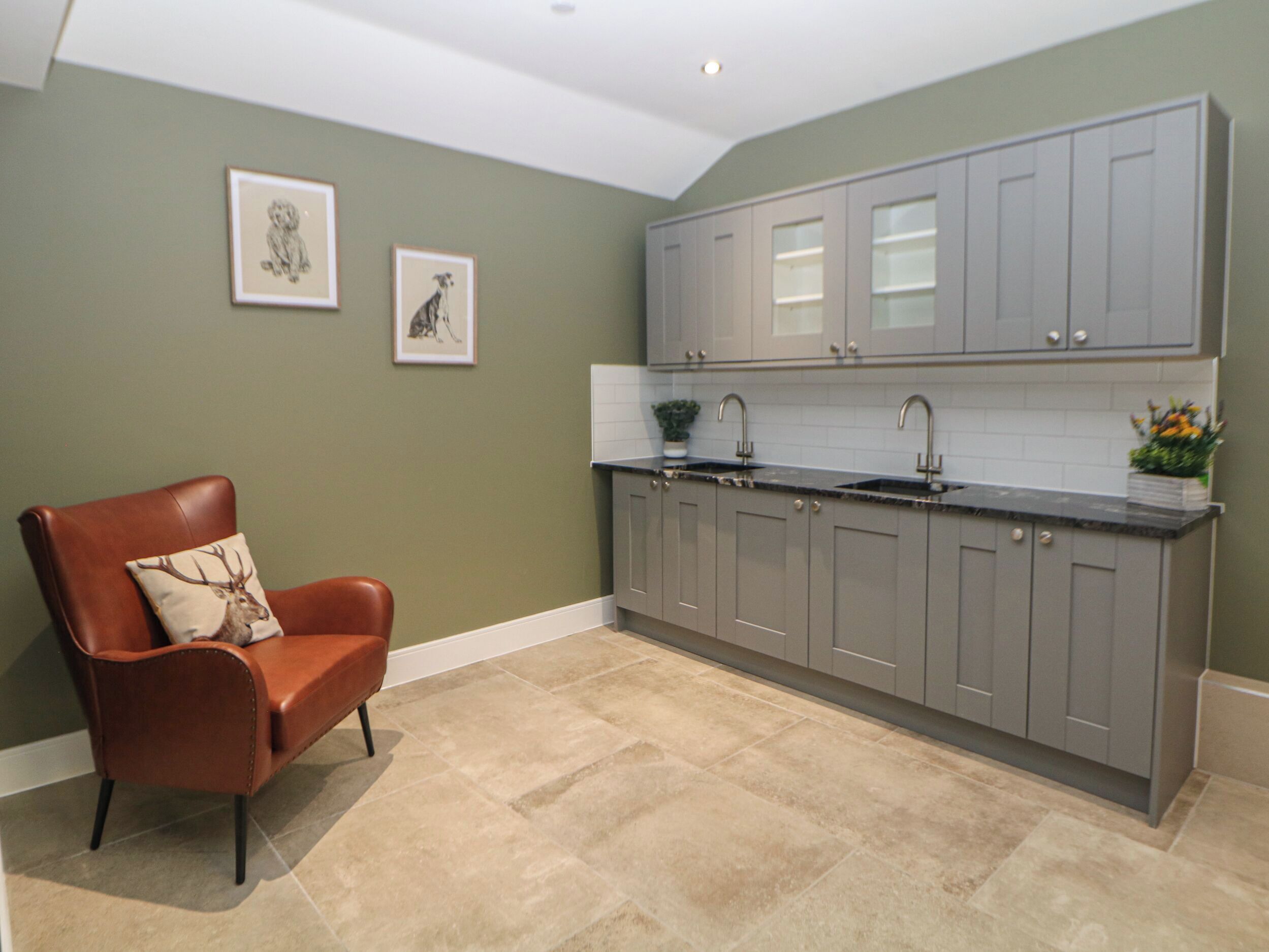 A kitchen with grey cabinets, a brown leather chair, and two framed pictures on the wall.