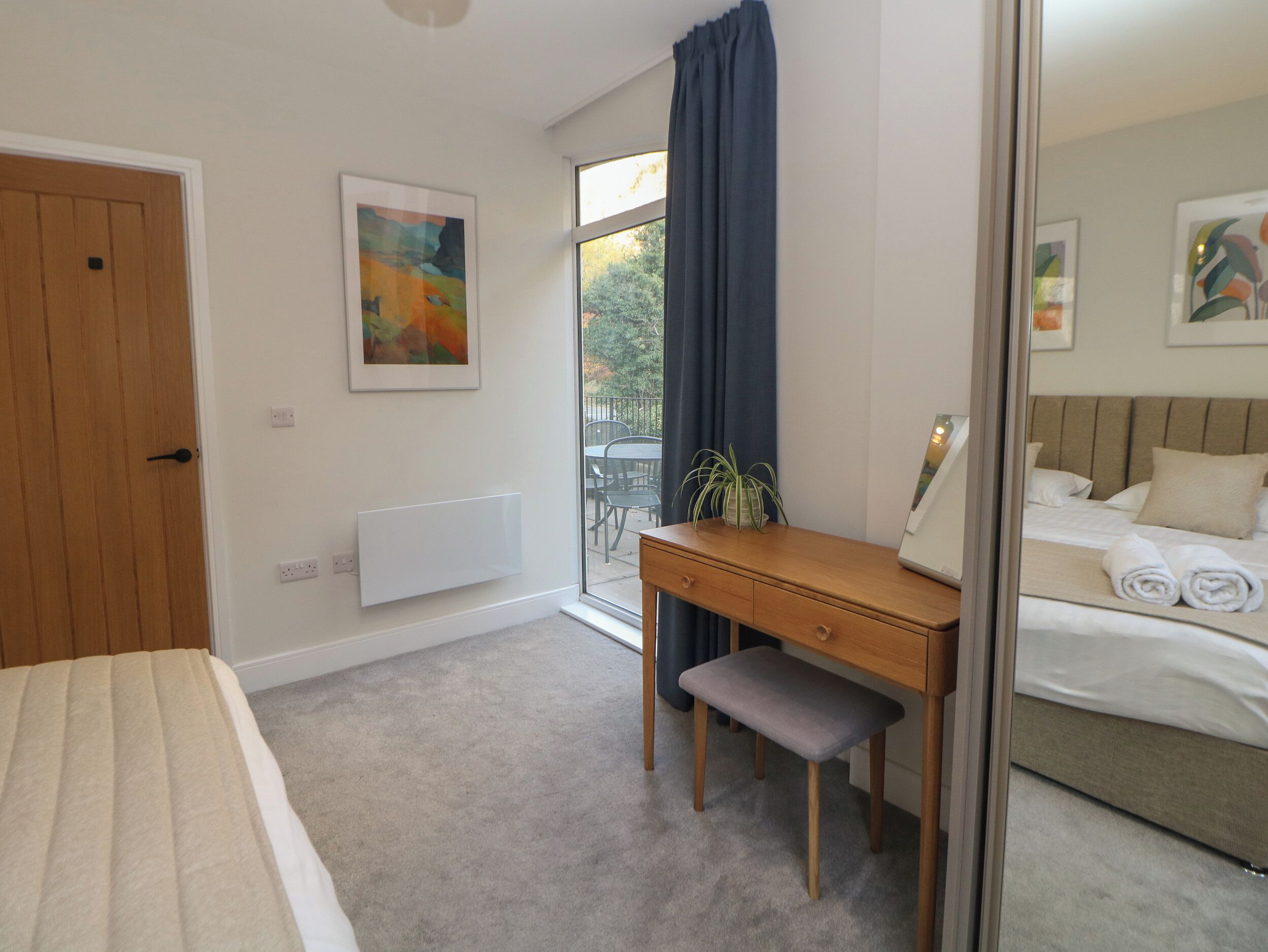 Une chambre à coucher avec un lit, un bureau avec une chaise, un radiateur, une fenêtre avec des rideaux et un tableau accroché au mur.