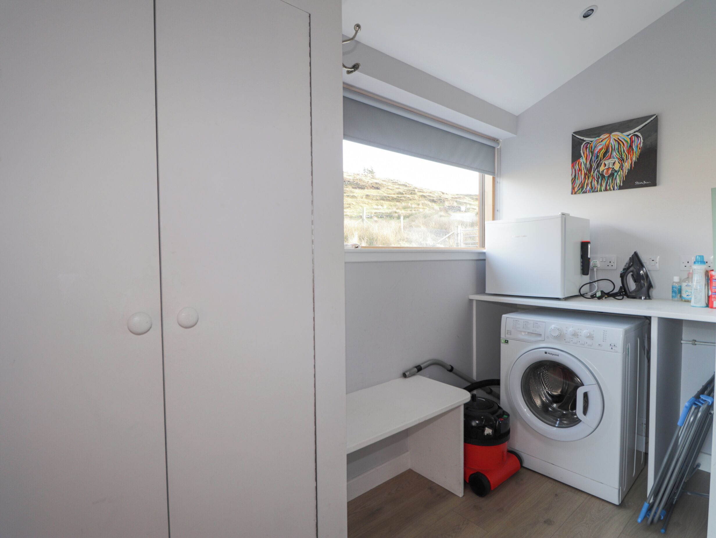 A laundry room with a washing machine, a vacuum cleaner, and a window with a view of the outdoors.