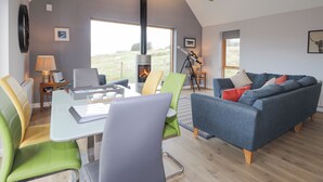 A cozy living room with a fireplace, a dining area, and a large window offering a view of the outdoors. - Skye Falls Chalet (Glendale)