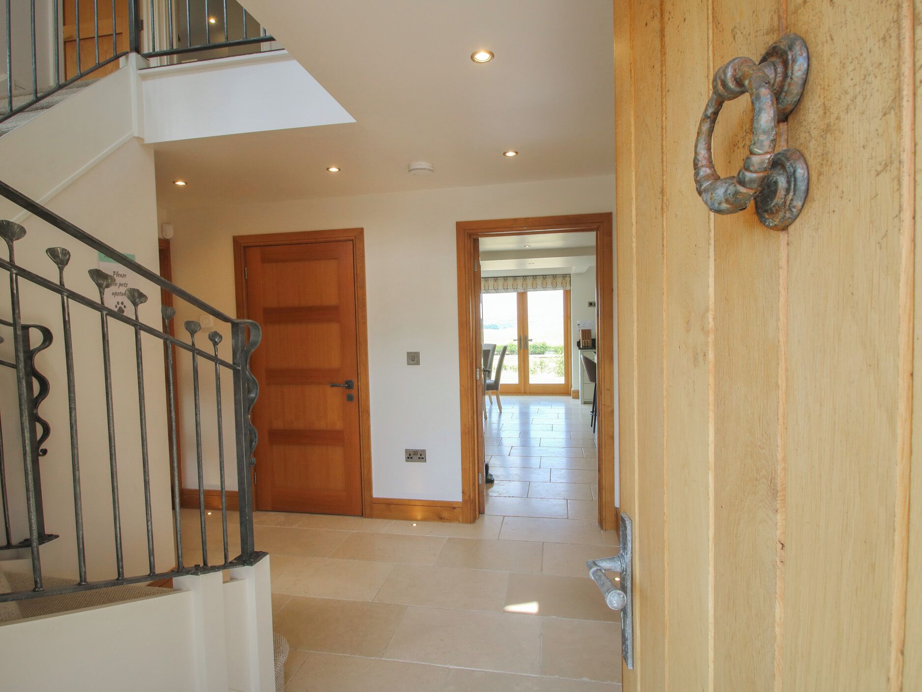 A spacious hallway with a wooden door, a metal railing, and a view into a dining area.