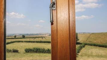 Een houten deur met een metalen handgreep, die uitkomt op een uitzicht over een landelijk gebied met velden en een omheining.