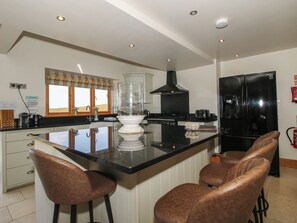 Una cocina con una isla central, taburetes de bar, un refrigerador negro y una ventana con vistas.