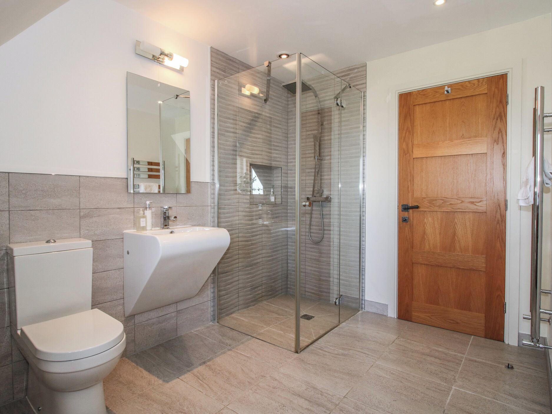 Un baño moderno con inodoro, lavabo, cabina de ducha de vidrio y puerta de madera.