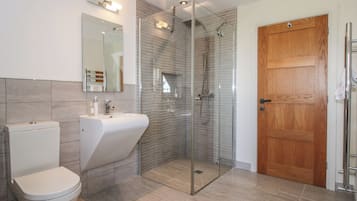 Un baño moderno con inodoro, lavabo, cabina de ducha de vidrio y puerta de madera.