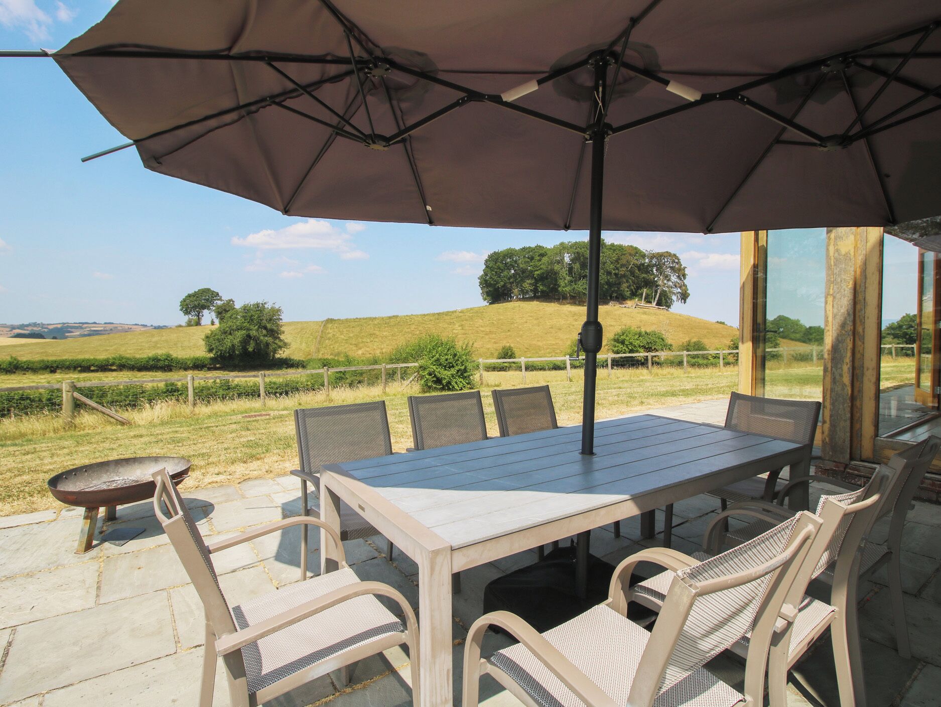 Une terrasse extérieure avec une table et des chaises, un barbecue et une vue sur un paysage vallonné.