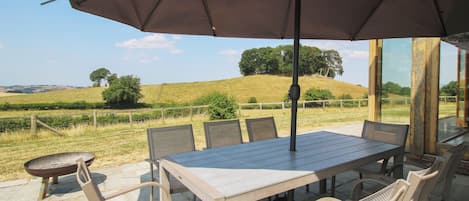 An outdoor patio with a table and chairs, a grill, and a view of a hilly landscape.