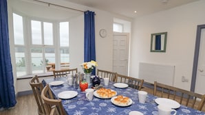 A dining room with a table set for six, featuring a blue tablecloth with nautical patterns, white plates, and a vase with flowers. - Fronwig (New Quay)