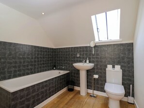 A modern bathroom with a bathtub, sink, toilet, and a window providing natural light. - Home Farm Barn (Moreton-in-Marsh)