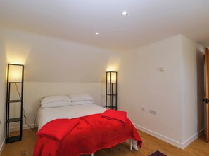 A bedroom with a bed, two bedside lamps, and a red blanket. - Home Farm Barn (Moreton-in-Marsh)