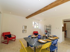 A dining area with a marble table, yellow and blue chairs, and red chairs with cushions. There are framed pictures on the wall and a window with a view. - Home Farm Barn (Moreton-in-Marsh)