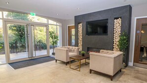 A modern lobby with a fireplace, two sofas, a coffee table, and a TV mounted on a marble wall. - 28 Rock Mill Holiday Apartments (Hope Valley)