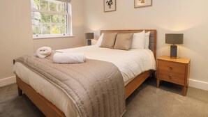 A bedroom with a large bed, two bedside tables, a window, and two wall-mounted plant pictures. - 28 Rock Mill Holiday Apartments (Hope Valley)