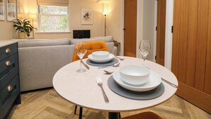 A dining area with a round table set for two, a sofa, and a TV in the background. - 28 Rock Mill Holiday Apartments (Hope Valley)