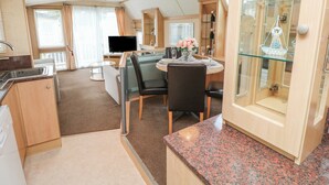 A compact kitchen with a granite countertop, a dining area with a glass table, and a TV in the background. - Seasalt Haven (Chichester)