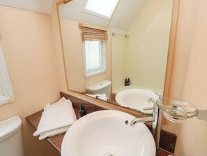 A bathroom with a white sink, a mirror, a toilet, and a bathtub. - Seasalt Haven (Chichester)