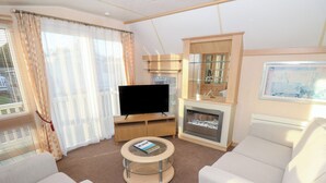 A modern living room with a flat-screen TV, a glass-top coffee table, and a fireplace. - Seasalt Haven (Chichester)