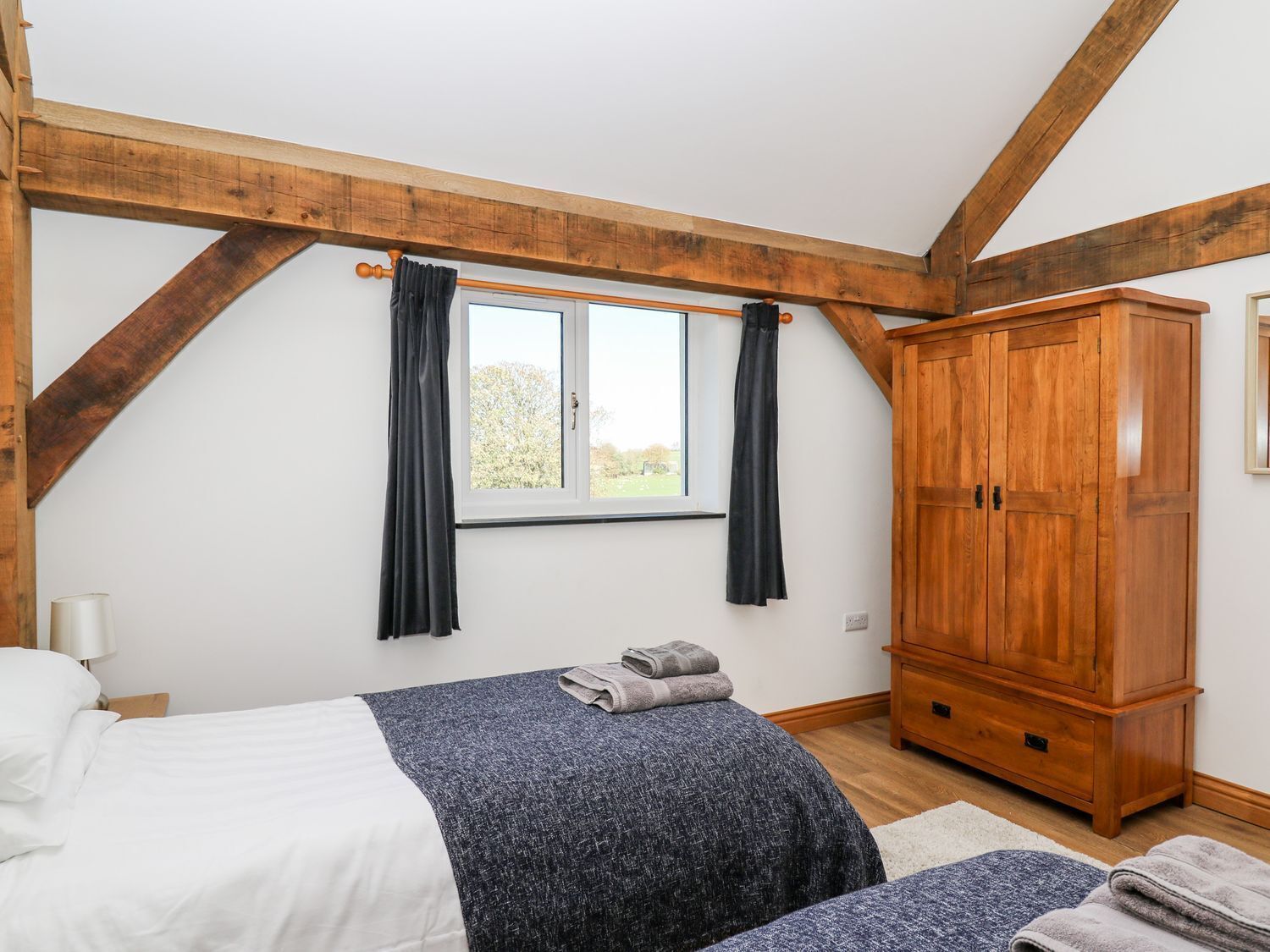A bedroom with a bed, a wardrobe, a window with curtains, and a view of the outdoors.