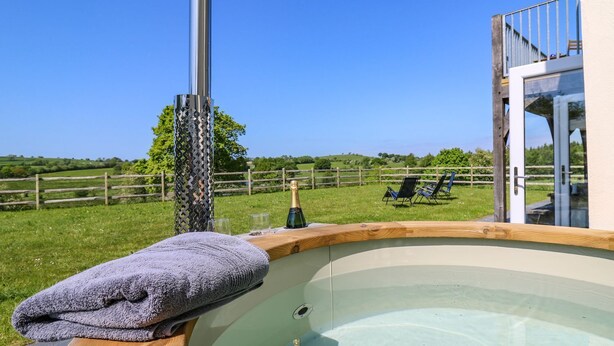 Un bain à remous avec une serviette, une bouteille de champagne et, en arrière-plan, une vue sur une clôture en bois et des chaises.