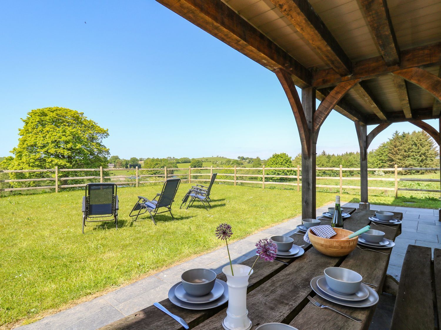 An outdoor dining area with a wooden table set for a meal, surrounded by a wooden fence and chairs.