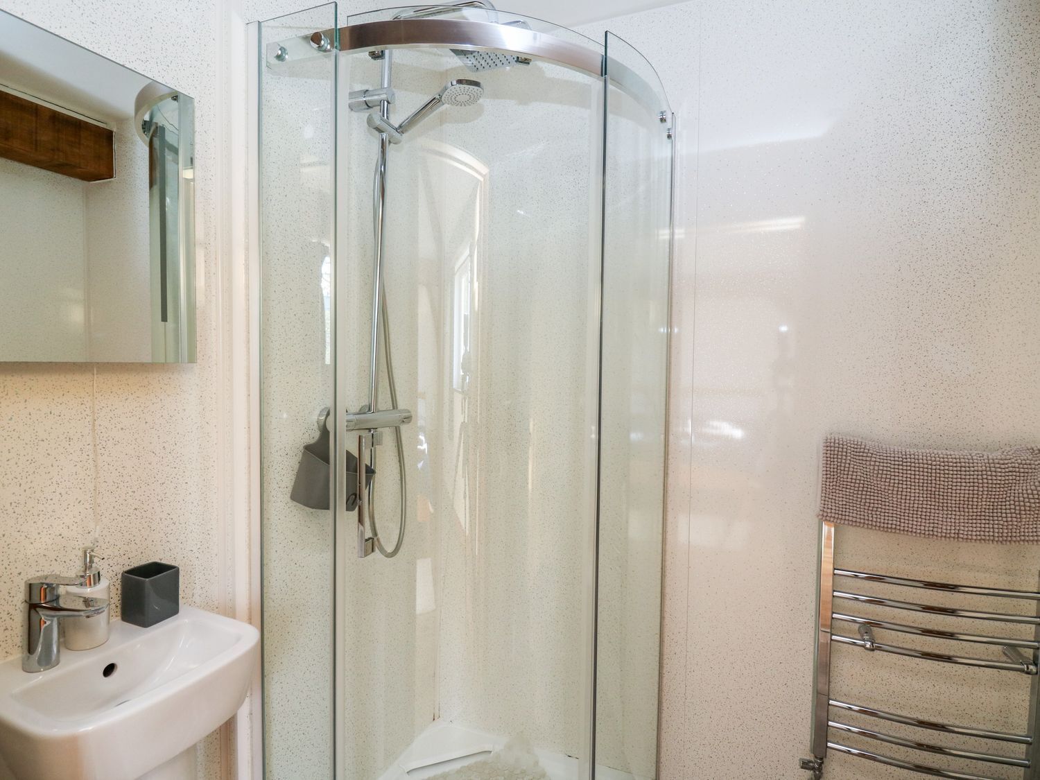 A modern bathroom with a glass-enclosed shower, a white sink, and a towel rack.