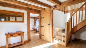 Une pièce spacieuse avec des poutres apparentes, un escalier et un coin repas à l’arrière-plan.