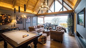 Amplia sala de estar con mesa de billar, sofás de cuero y un ventanal con vistas al exterior.