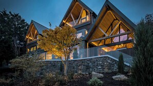 Una casa moderna con base de piedra, ventanas amplias y una llamativa estructura de techo triangular.