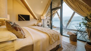 Un dormitorio con una cama grande, televisión y vista a un lago a través de un ventanal.