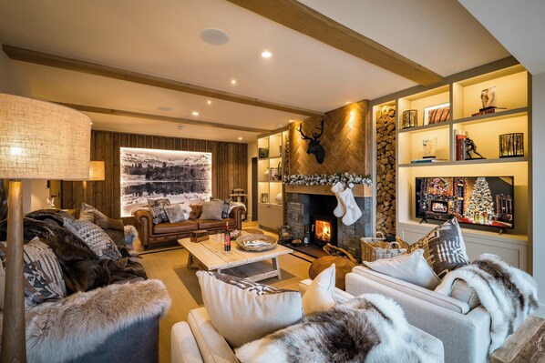 A cozy living room with a fireplace, plush sofas, and a large wall-mounted television. - The Ridge (Windermere)