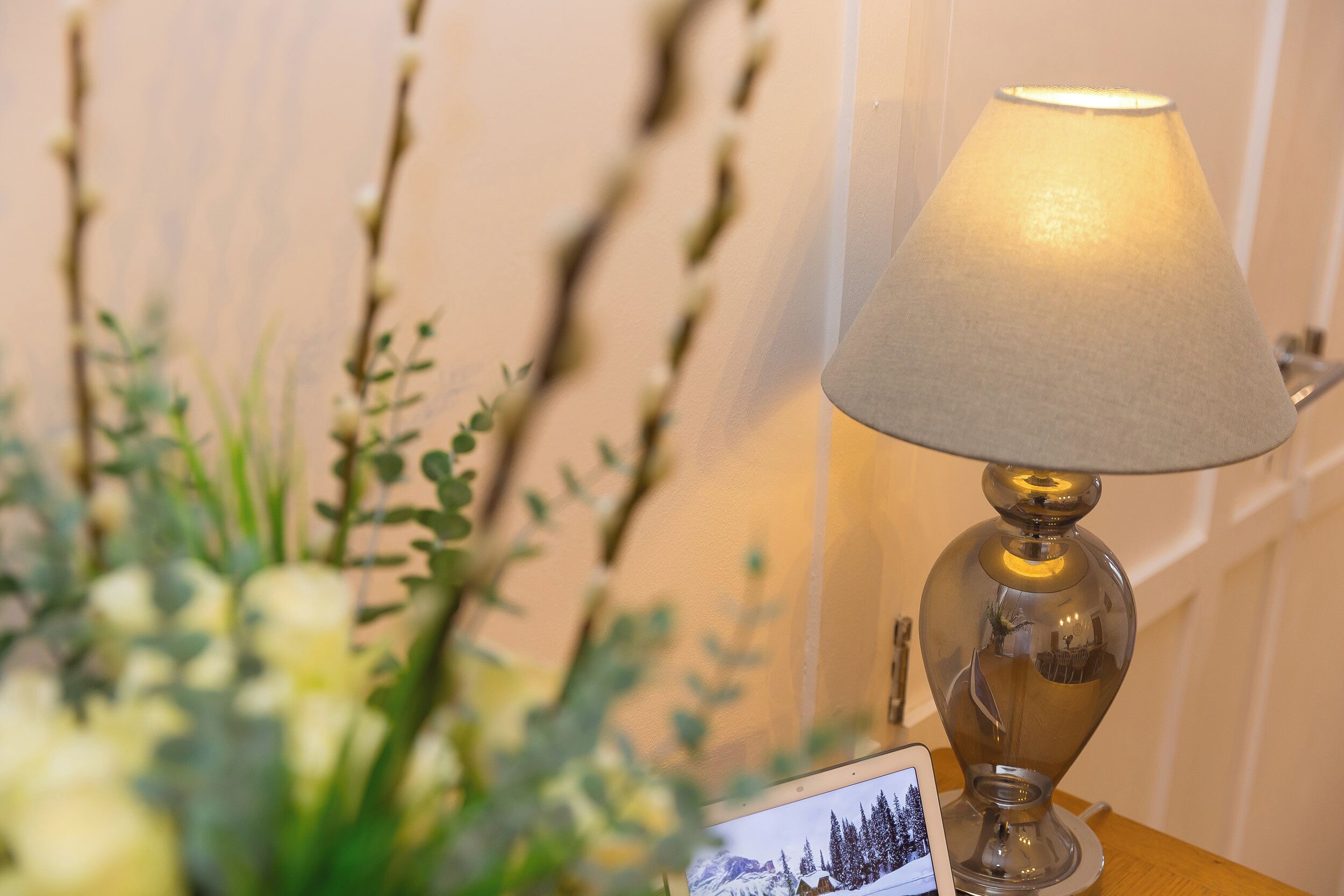 A table lamp with a clear shade, a framed photograph, and a vase with green foliage.