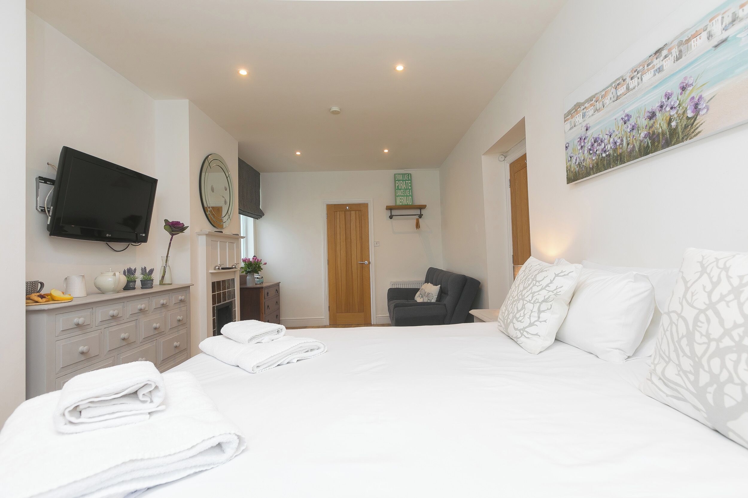 A bedroom with a bed, a TV, a dresser, a chair, and a door leading to another room.