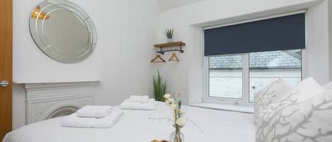 Ein Schlafzimmer mit einem Bett, einem Nachttisch, einem Spiegel, einem Fenster mit Blick und einer kleinen Ablage mit einer Pflanze.